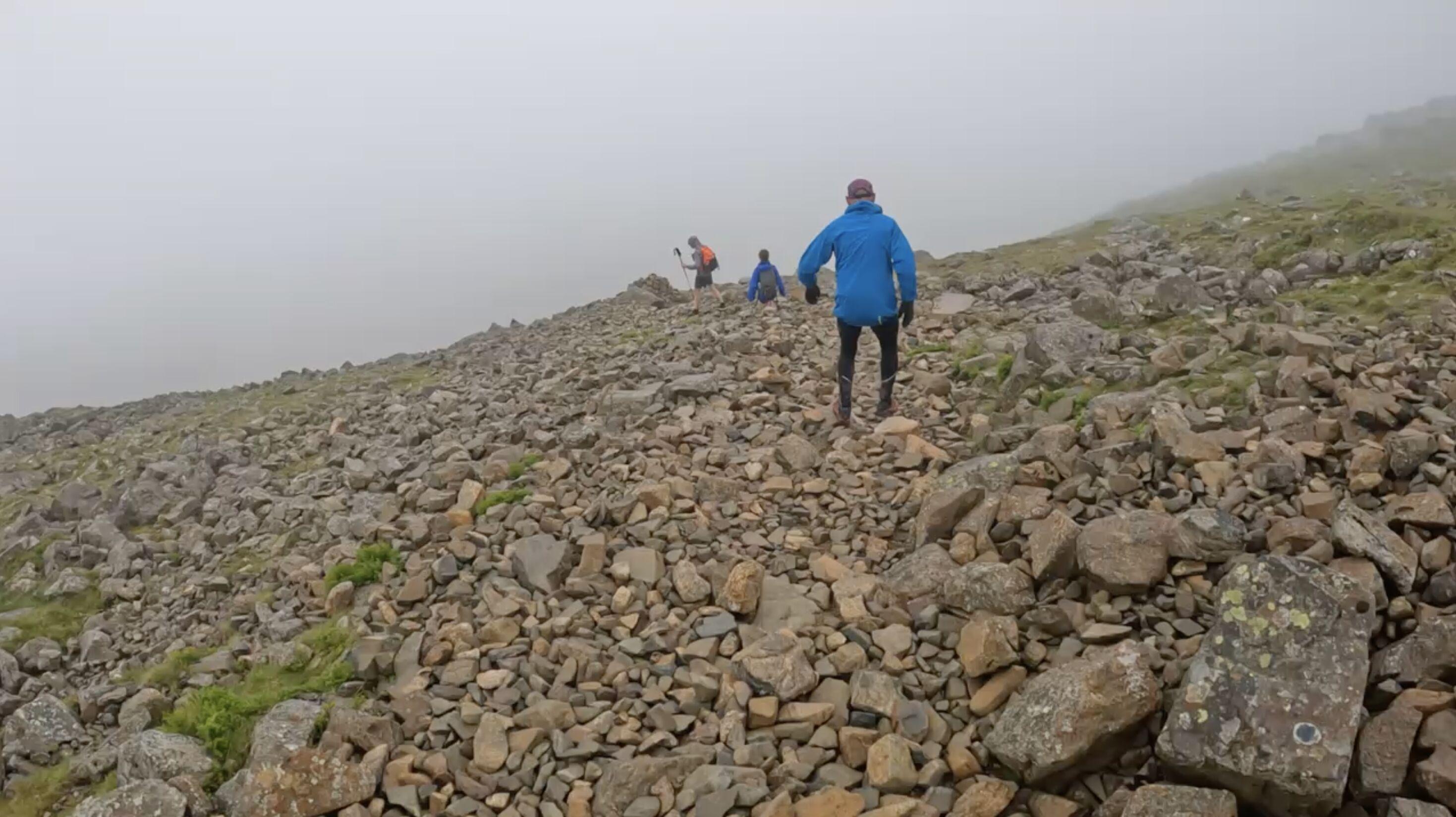Three fell runners crossing a field of yellowish stones, descending into a thick fog in the distance