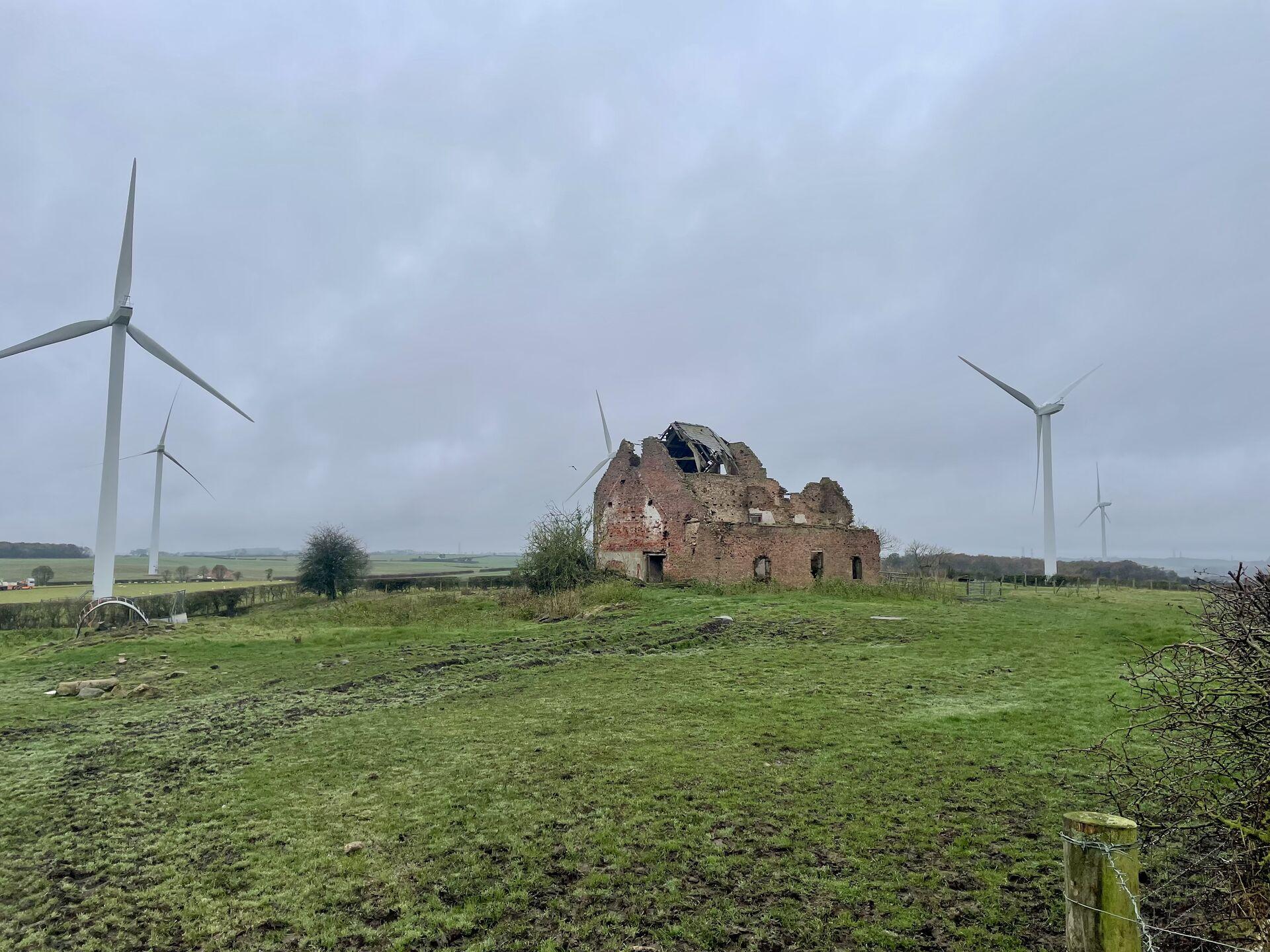 A ruined cottage stands in a grassy field full of wind turbines