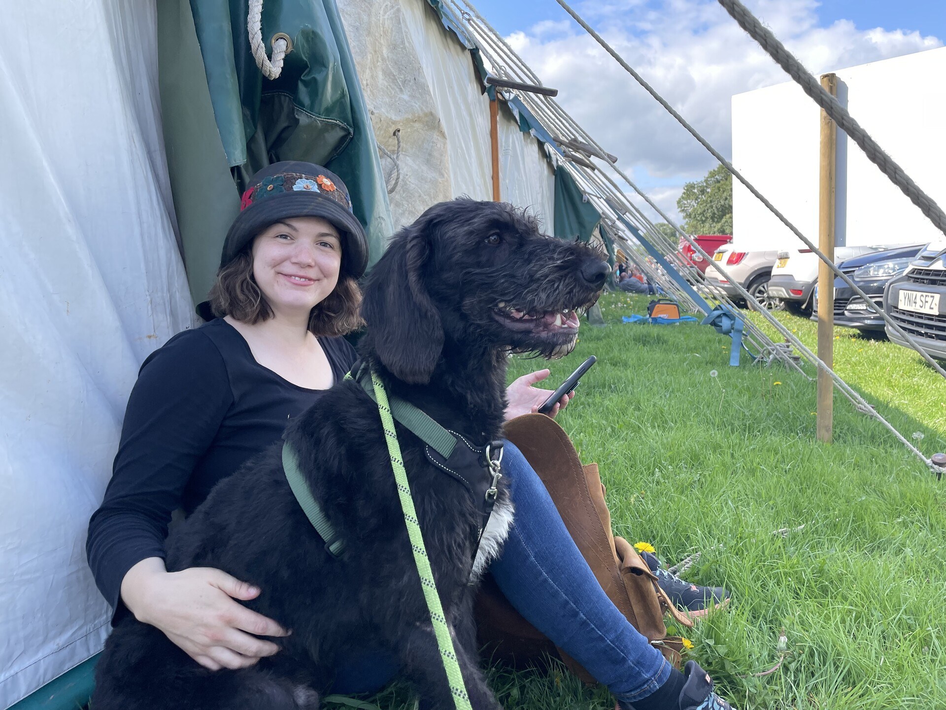 Sam and Ghyll sitting together on the grass in the shade of a big canvas tent.