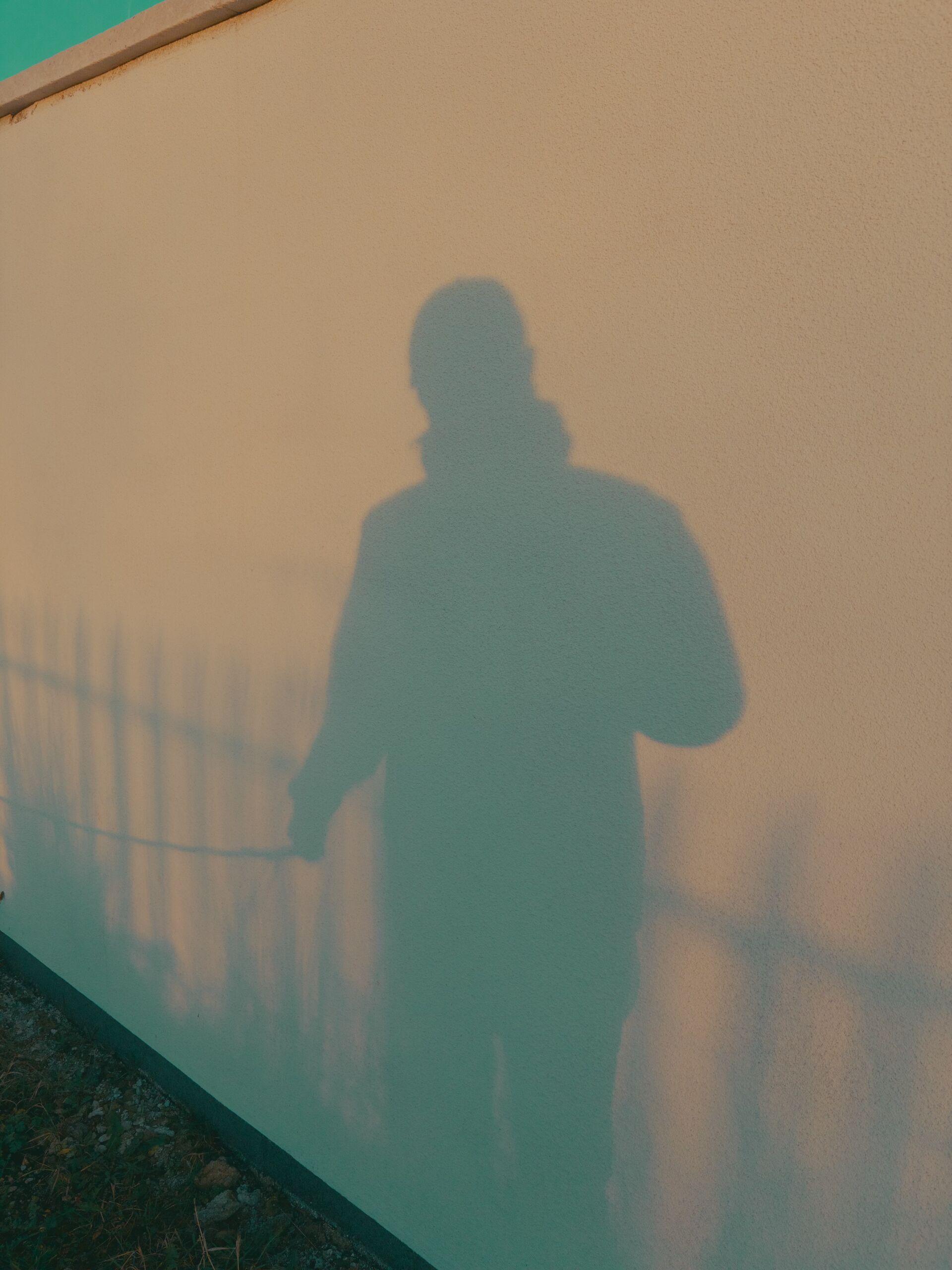 A photographer's shadow projected on a white wall, with a lead in the shadow's hand leading off-frame to the left