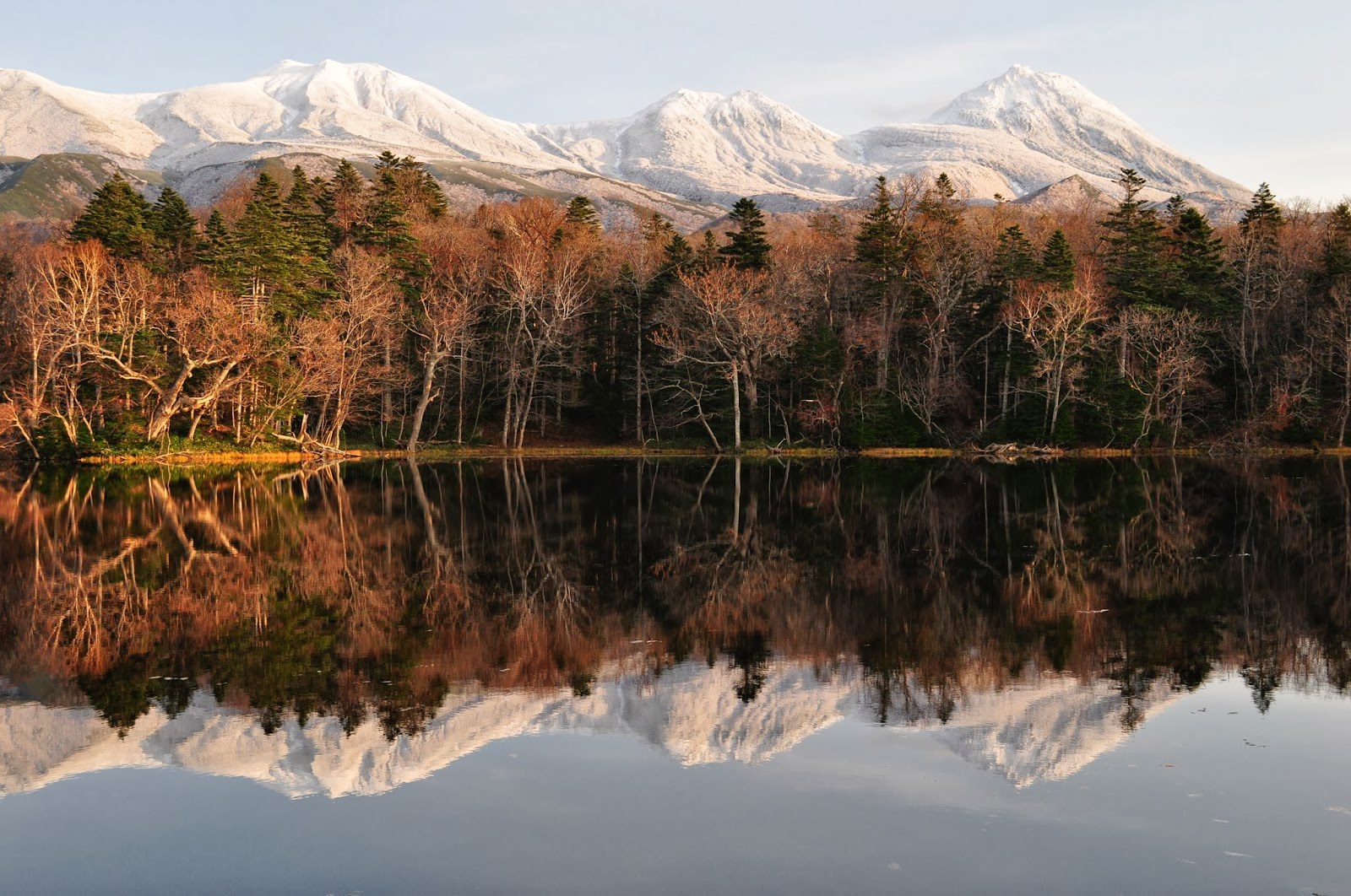The snow-capped mountains of Shiretoko rising above the trees on the far side of a totally still lil tarn