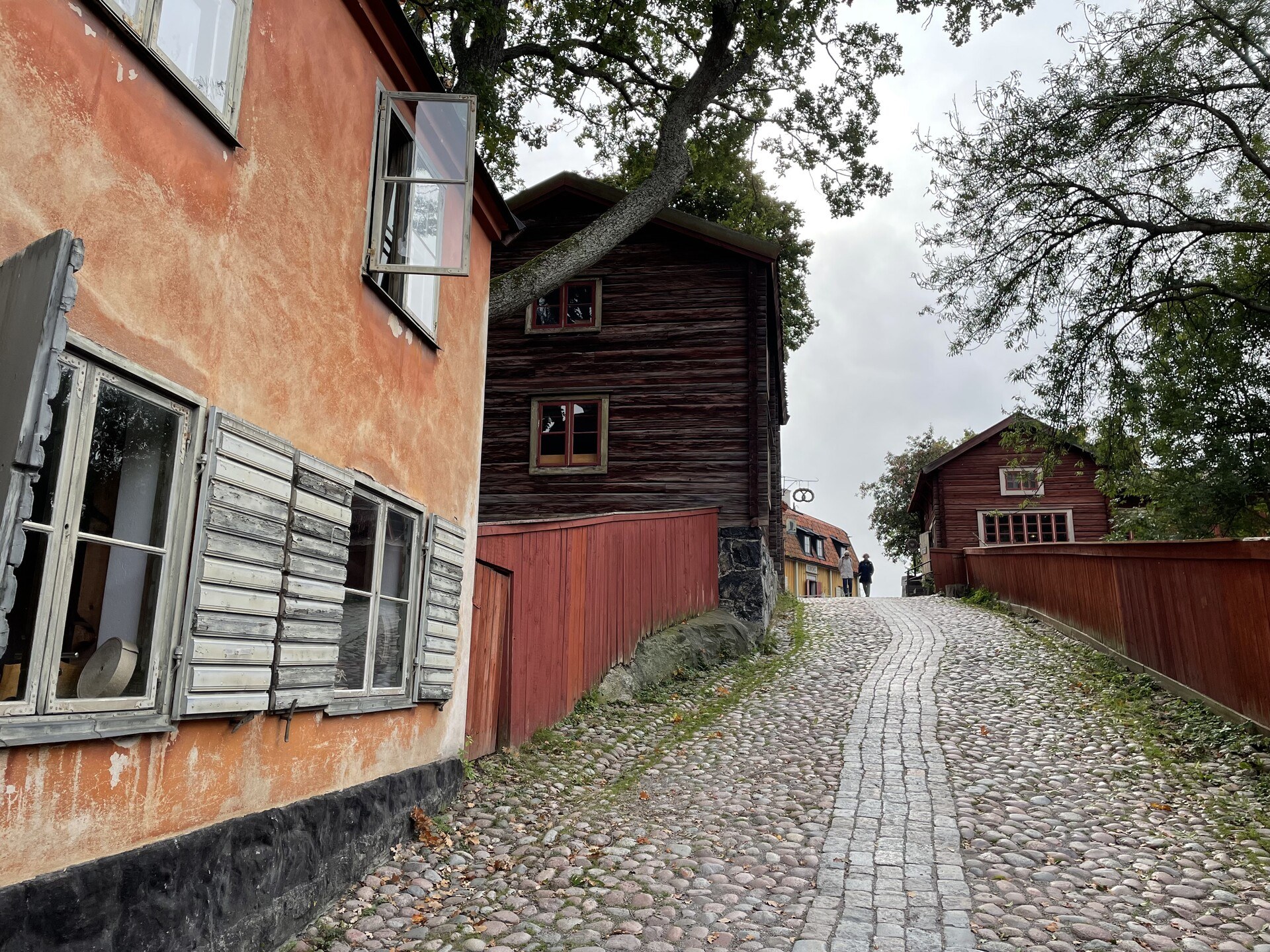 A cobblestone street heading up a hill with old houses on the left and a low fence on the right