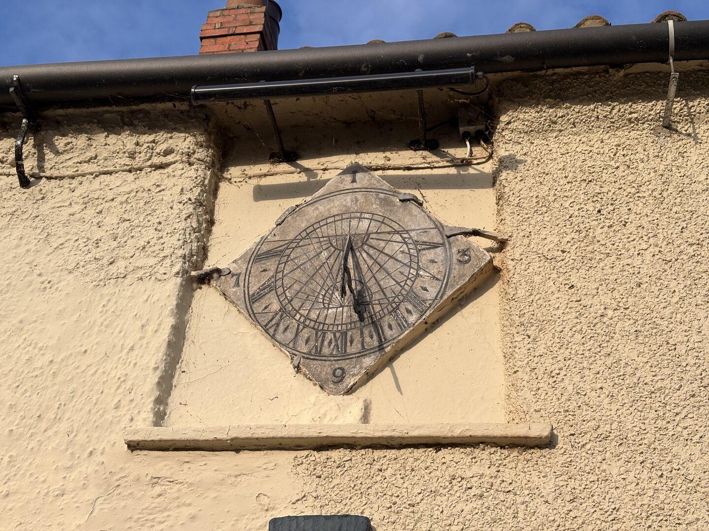 A sundial mounted under the eaves of a rendered building, indicating shortly after 2pm (correctly!)
