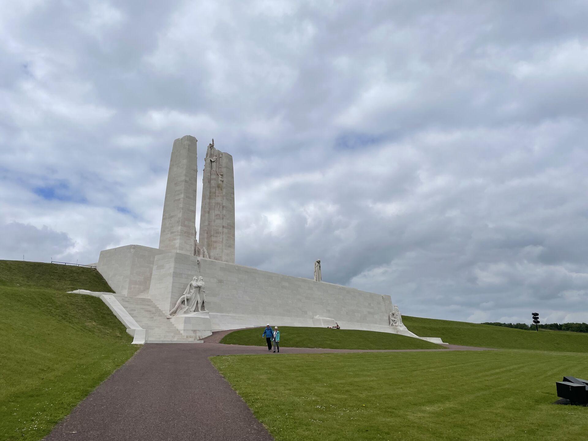 Two white towers reaching up into a cloudy sky, set on a white plinth with a manicured lawn stretching out in front of it, viewed from the side