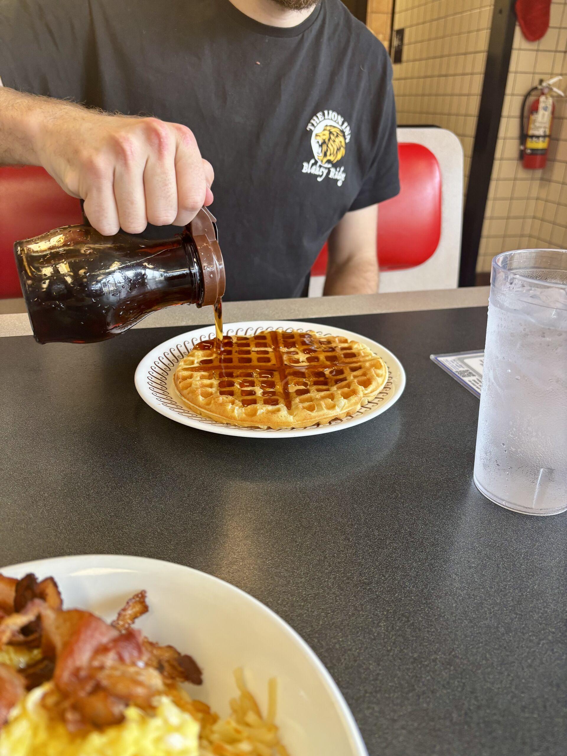 Pouring a thick syrup onto a waffle on a diner-style booth table