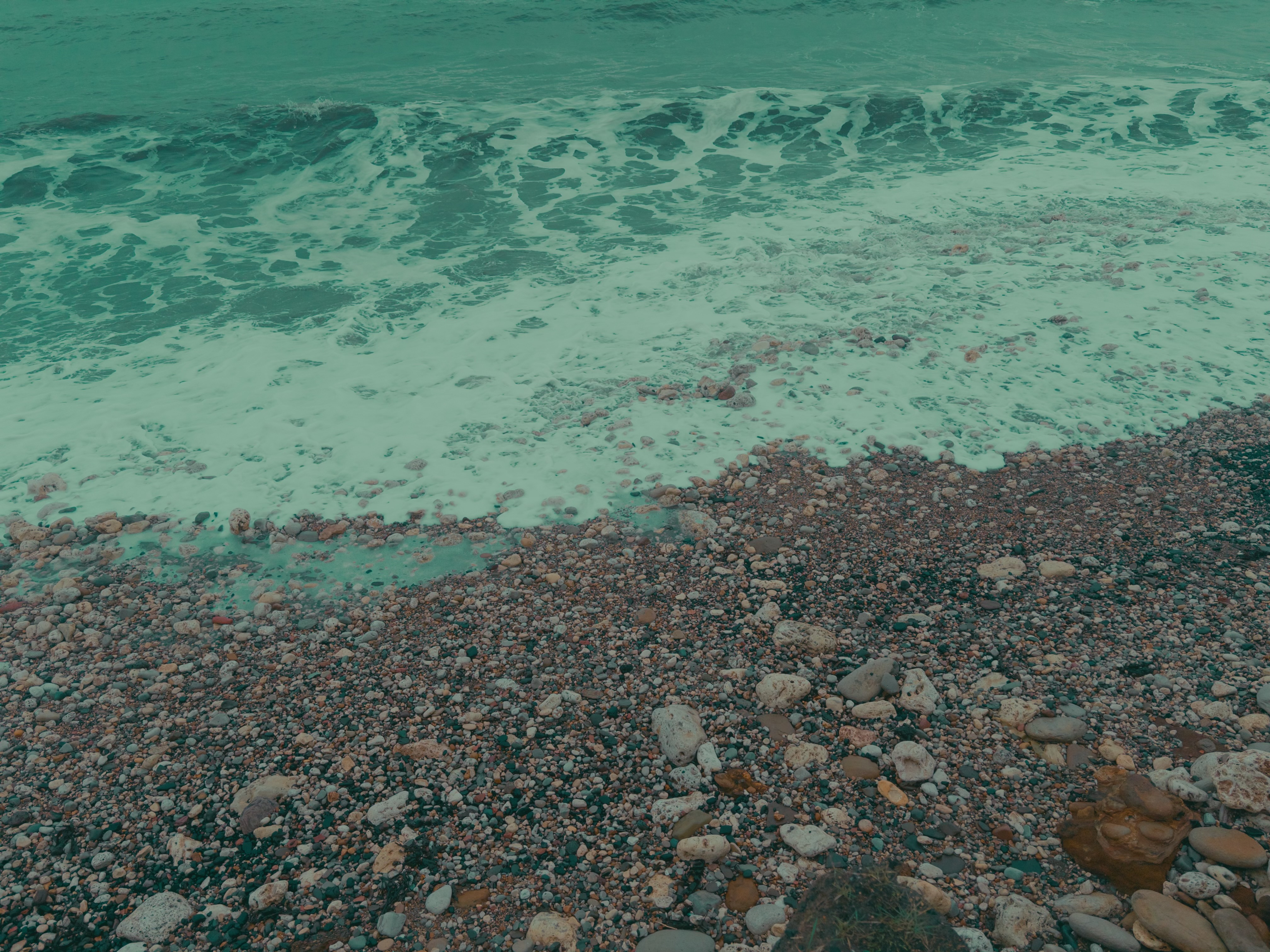 A wave crashing on a stony shore, foaming as it recedes.