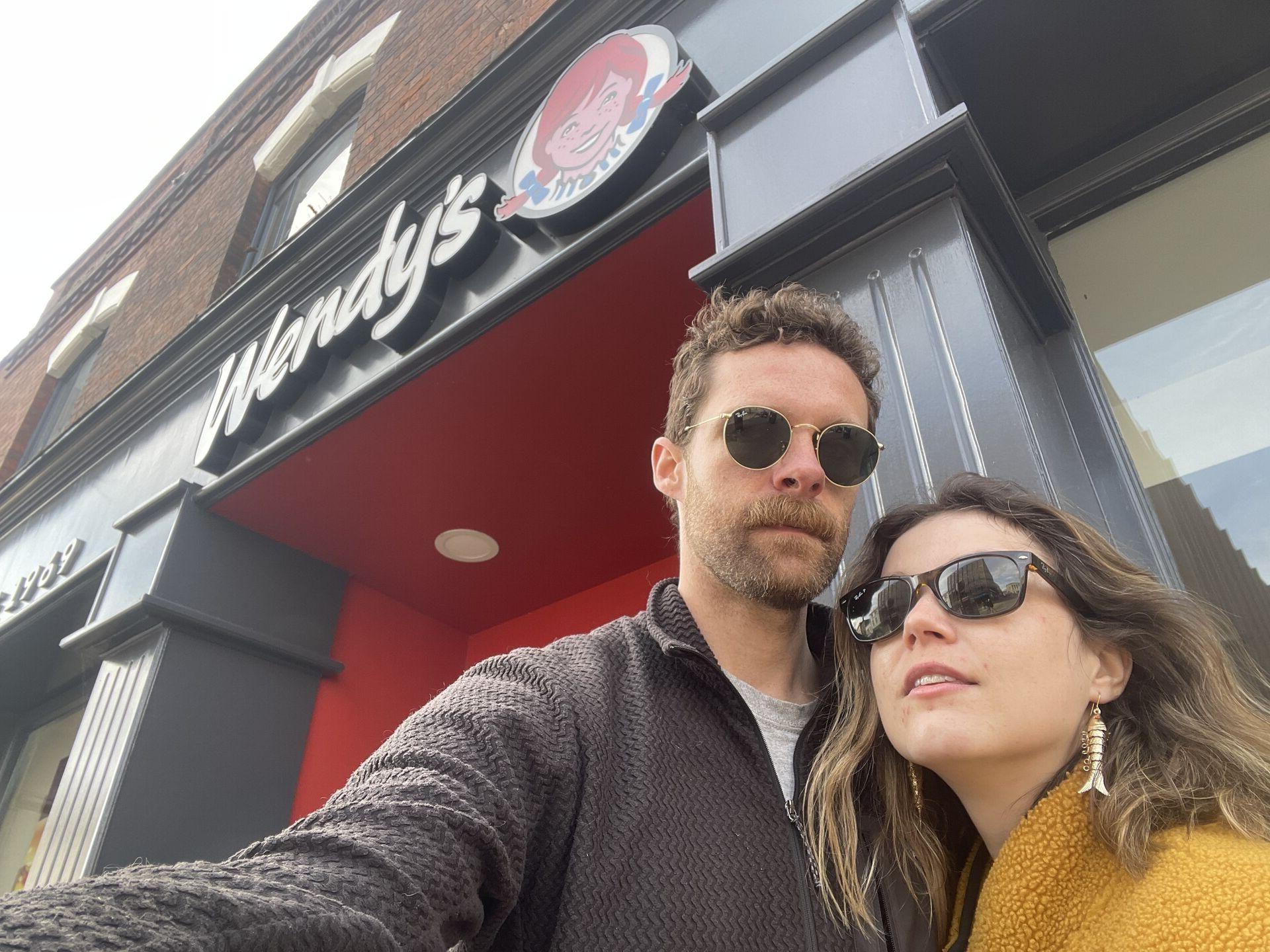 Two people posing dramatically for a selfie in front of a Wendy's restaurant