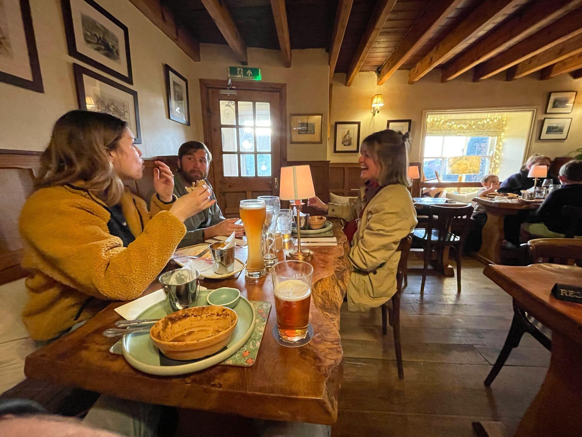 Three people sitting and eating at a wooden table in a cozy country pub with framed pictures on the walls