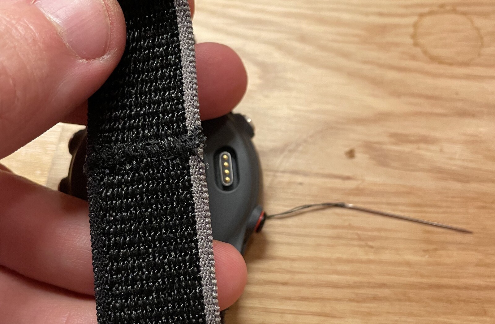 Holding a fabric watch wristband up to the camera, which has clearly been cut in half and stitched back together, albeit poorly
